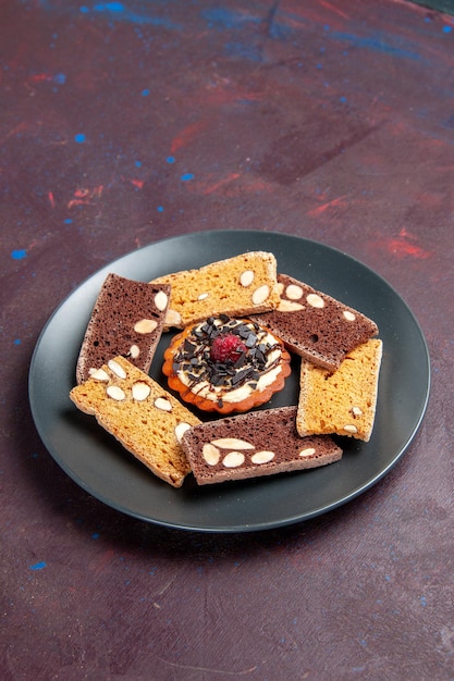 Foto gratuita vista frontal deliciosas rebanadas de pastel con nueces y galleta pequeña en el espacio oscuro