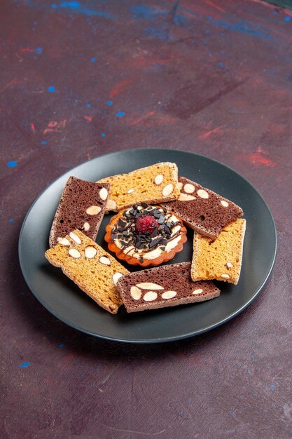 Vista frontal deliciosas rebanadas de pastel con nueces y galleta pequeña en el espacio oscuro