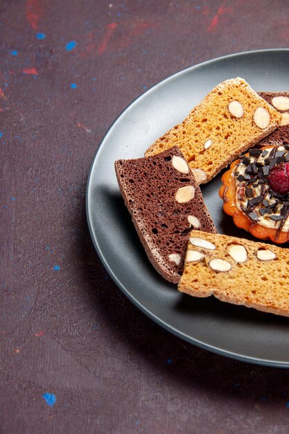 Vista frontal deliciosas rebanadas de pastel con nueces y galleta pequeña en el espacio oscuro