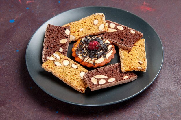 Vista frontal deliciosas rebanadas de pastel con nueces y galleta pequeña en el espacio oscuro