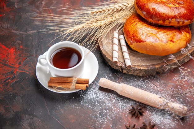 Vista frontal deliciosas tartas con taza de té en una mesa oscura pastel pastelería tarta dulce