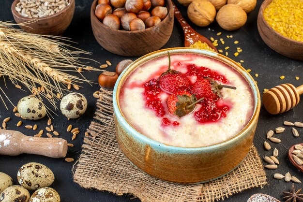 Vista frontal del delicioso desayuno servido con mermelada de fresas en un tazón y avellanas huevos nueces arroz amarillo sobre fondo de color oscuro