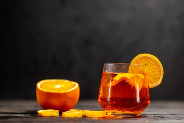 Vista frontal del delicioso jugo natural fresco en un vaso con limas de naranja en la mesa oscura