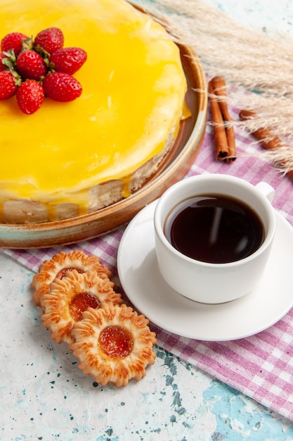 Vista frontal delicioso pastel con almíbar amarillo fresas rojas frescas y taza de té sobre superficie azul