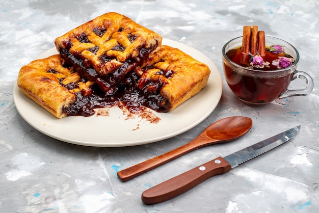 Una vista frontal delicioso pastel de cerezas y afrutado dentro de la placa blanca junto con té en el escritorio oscuro pastel de fruta de galleta