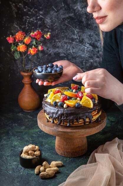 Vista frontal delicioso pastel de chocolate decorado con frutas frescas por mujer en pared oscura