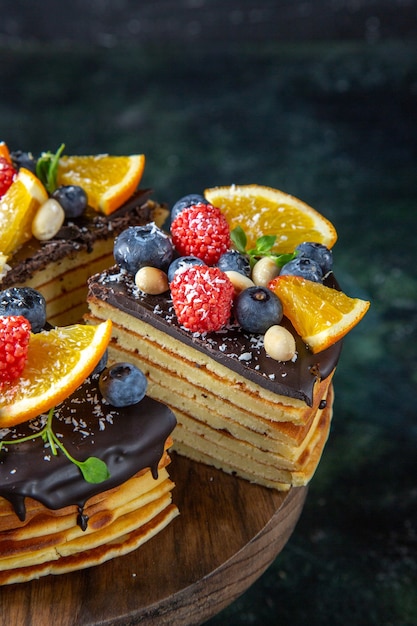Vista frontal delicioso pastel de chocolate con frutas en la pared oscura