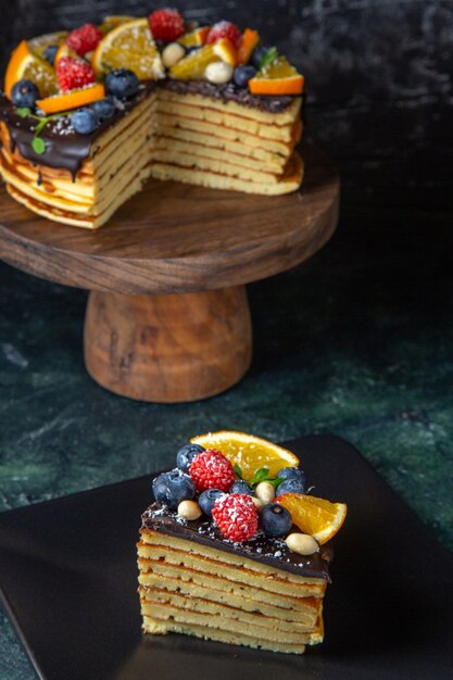 Vista frontal delicioso pastel de chocolate con frutas en la pared oscura