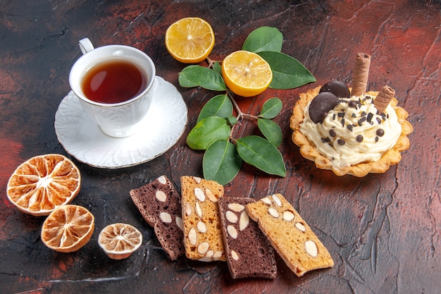 Vista frontal delicioso pastel cremoso con taza de té sobre fondo oscuro