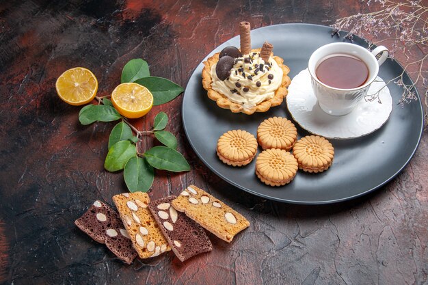 Vista frontal delicioso pastel cremoso con té en el postre de pastel dulce de mesa oscura