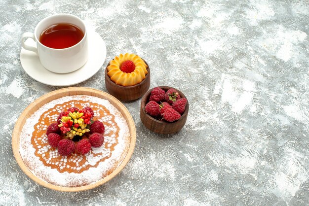 Vista frontal delicioso pastel de frambuesa con una taza de té sobre fondo blanco, té de galletas, pastel de tarta dulce de azúcar