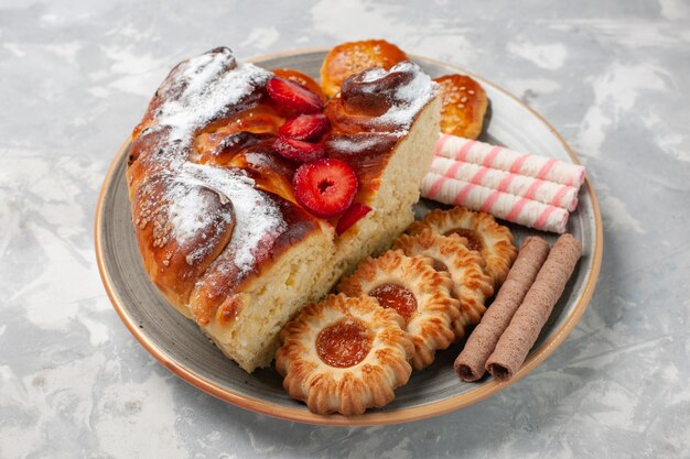 Vista frontal del delicioso pastel de fresa con galletas y pasteles en el escritorio blanco