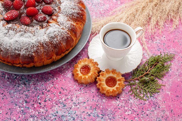 Vista frontal delicioso pastel de fresa con galletas y taza de té en la superficie rosa pastel pastel de galletas de azúcar dulce