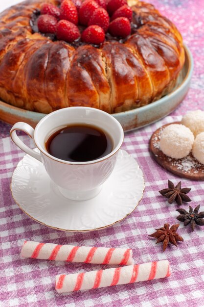 Vista frontal delicioso pastel de fresa con taza de té en rosa