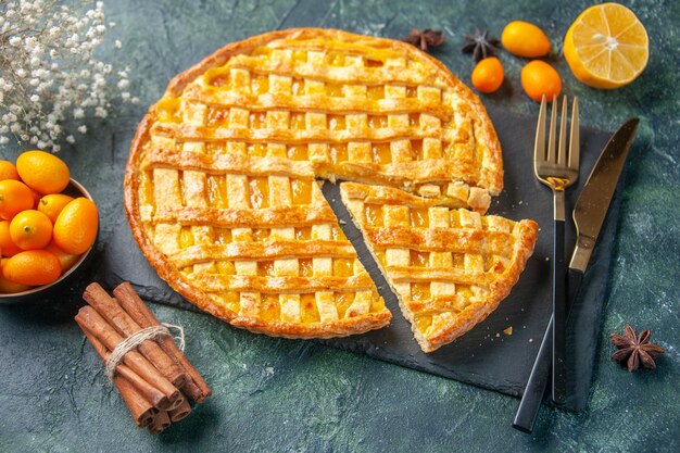 Vista frontal delicioso pastel de kumquat con una pieza en rodajas sobre una superficie oscura postre dulce hornear galletas de té de masa de pastel de horno de color galleta