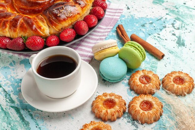 Vista frontal delicioso pastel con macarons de fresas y una taza de té en la superficie azul galleta pastel galleta dulce pastel de caramelo
