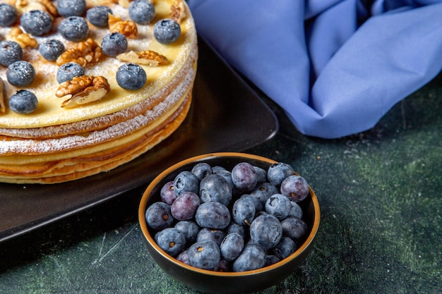 Vista frontal delicioso pastel de miel con arándanos y nueces dentro de la superficie oscura de la placa