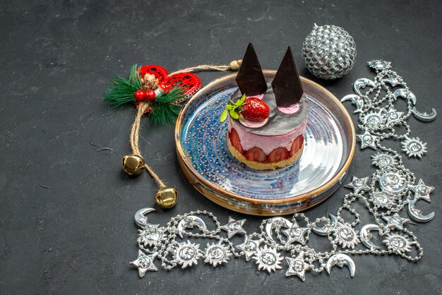 Vista frontal delicioso pastel de queso con fresa y chocolate en placa ovalada adorno de Navidad sobre fondo oscuro aislado lugar libre
