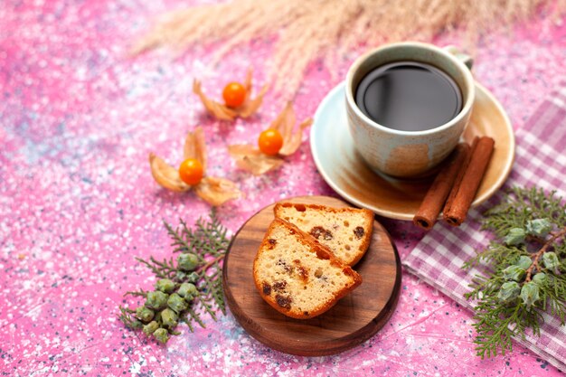 Vista frontal delicioso pastel en rodajas con una taza de té y canela en el escritorio rosa.