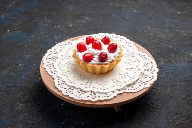 Vista frontal delicioso pastelito con crema y frutos rojos en la superficie oscura fruta dulce