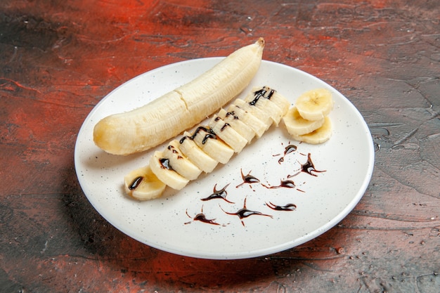 Vista frontal delicioso plátano con trozos en rodajas dentro de la placa sobre fondo oscuro color de fruta de sabor de árbol fotográfico