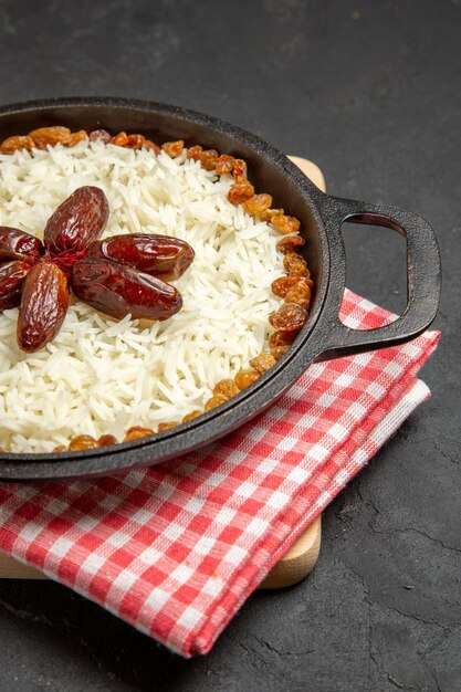 Vista frontal delicioso plato de arroz cocido plov con pasas en la superficie oscura plato de pasas cena de arroz comida de aceite