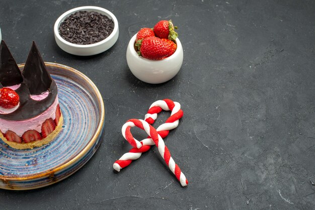 Vista frontal delicioso tarta de queso con fresa y chocolate en tazones de fuente con fresas dulces de Navidad de chocolate sobre fondo oscuro aislado con lugar de copia