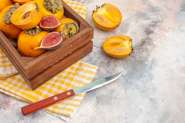 Vista frontal deliciosos caquis e higos cortados en caja de madera toalla de cocina amarilla un cuchillo en el espacio libre desnudo
