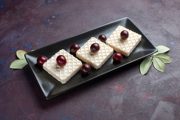 Vista frontal deliciosos gofres con cerezas dentro de la placa sobre la superficie oscura