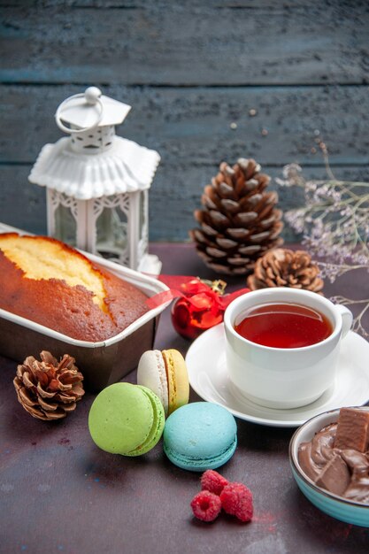 Vista frontal deliciosos macarons franceses con chocolate y una taza de té sobre fondo oscuro galleta tarta pastel de té dulce galleta