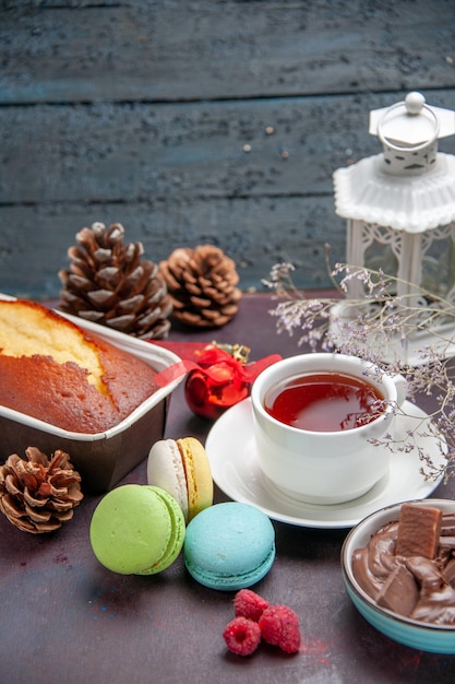 Vista frontal deliciosos macarons franceses con chocolate y una taza de té sobre fondo oscuro galleta tarta pastel de té dulce galleta