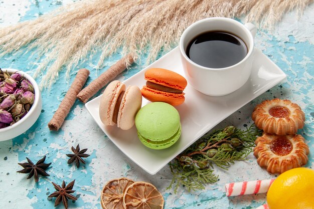 Vista frontal deliciosos macarons franceses con taza de té y galletas en superficie azul