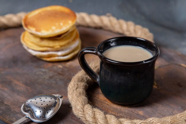 Vista frontal deliciosos muffins deliciosos y horneados con una taza de leche negra sobre el fondo gris comida desayuno azúcar dulce