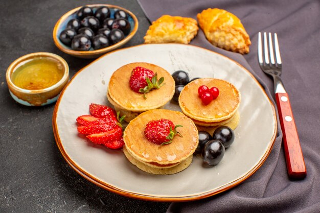 Vista frontal deliciosos panqueques con aceitunas y frutas sobre piso oscuro pastel de frutas dulces