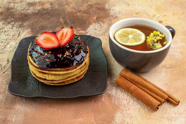 Vista frontal deliciosos panqueques dulces con taza de té en la mesa de luz pastel dulce postre leche