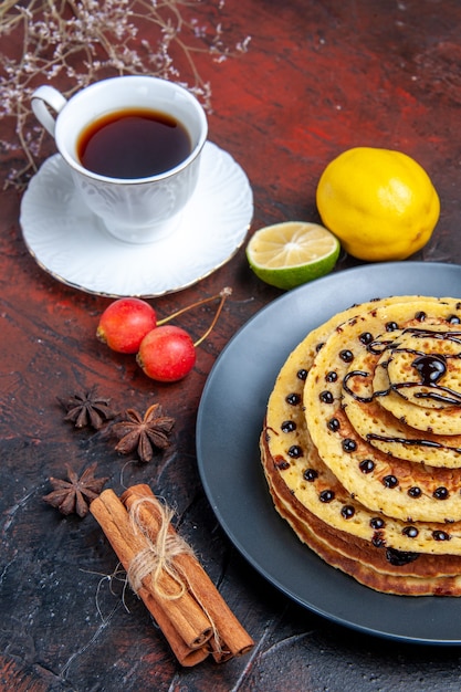 Foto gratuita vista frontal deliciosos panqueques dulces con taza de té sobre un fondo oscuro pastel dulce postre de leche