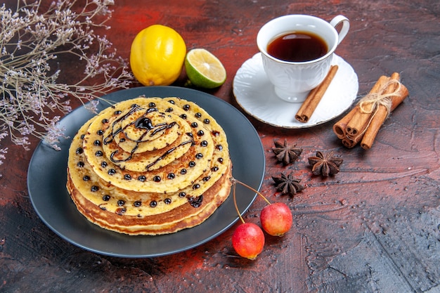 Vista frontal deliciosos panqueques dulces con taza de té sobre fondo oscuro postre dulce de leche de pastel