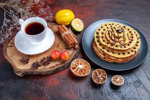 Vista frontal deliciosos panqueques dulces con taza de té sobre fondo oscuro postre dulce de leche de pastel