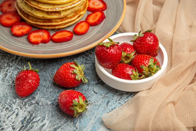 Vista frontal deliciosos panqueques con fresas frescas en superficie ligera pastel dulce fruta