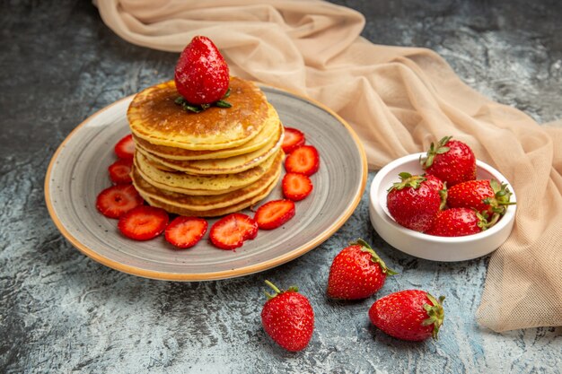 Vista frontal deliciosos panqueques con fresas frescas en superficie ligera pastel dulce fruta