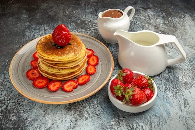 Vista frontal deliciosos panqueques con fresas y miel en la superficie clara de la fruta dulce de la torta