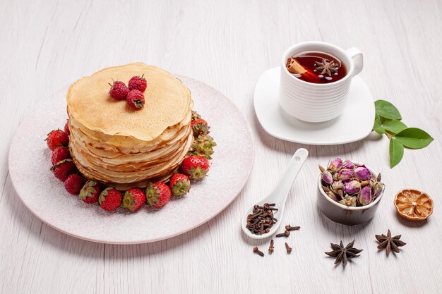 Vista frontal deliciosos panqueques con fresas y una taza de té en el espacio en blanco