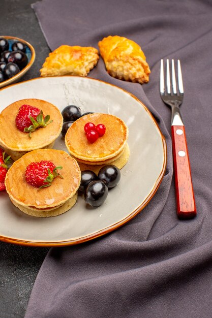 Vista frontal deliciosos panqueques con frutas y aceitunas en la superficie oscura pastel de frutas dulces