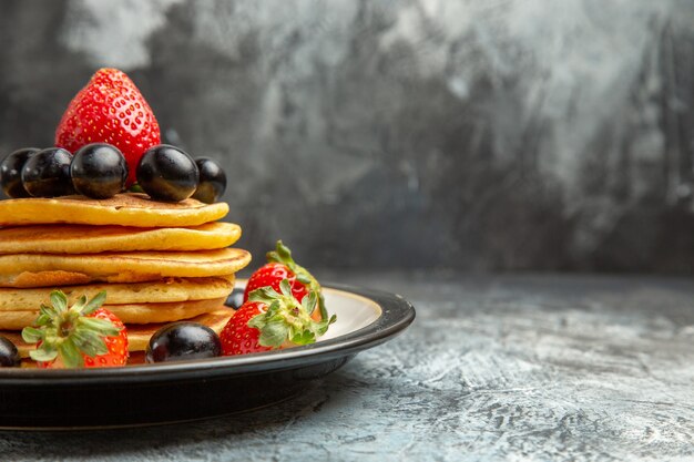 Vista frontal deliciosos panqueques con frutas y bayas en el postre de pastel de frutas de superficie oscura