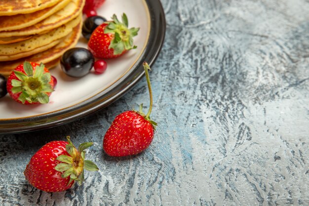 Vista frontal deliciosos panqueques con frutas y bayas en la superficie ligera pastel de frutas dulce