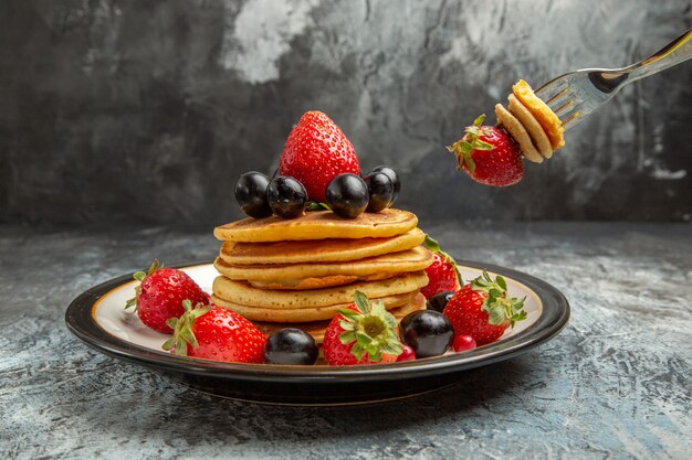 Vista frontal deliciosos panqueques con frutas y bayas en la superficie oscura pastel de frutas de postre