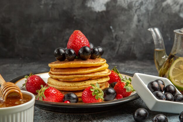 Vista frontal deliciosos panqueques con frutas frescas en la superficie de la luz pastel dulce de frutas