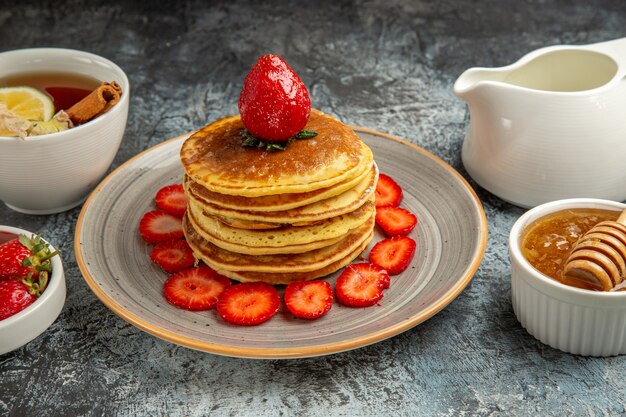 Vista frontal deliciosos panqueques con frutas y miel en frutas de pastel dulce de superficie ligera