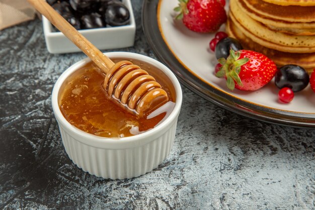 Vista frontal deliciosos panqueques con frutas y miel en superficie ligera pastel de frutas dulce