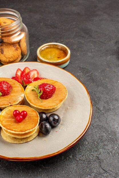 Vista frontal deliciosos panqueques con frutas sobre superficie oscura pastel de frutas pastel dulce